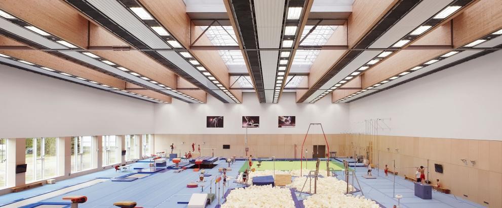 Innenaufnahme einer modernen Turnhalle des olympischen und paralympischen Trainingszentrums in Grünheide mit verschiedenen Turngeräten wie Sprungtische, Schwebebalken und Barren. Realisierung eines klimaneutralen Energiekonzeptes für das Trainingszentrum.